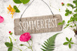 Sommerfest - Einladung / Karte mit Holzschild und verschiedenen Pflanzen (Erdbeerstaude, Rose, Farn, Geißblatt) auf einem rustikalen weißen Holz Hintergrund, top view