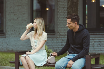 Wall Mural - man pickpocketing smartphone from bag of woman drinking coffee to go on bench in park