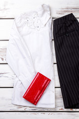 Wall Mural - Folded white decorated women blouse and red wallet. Black striped trousers. Wooden desks surface background.