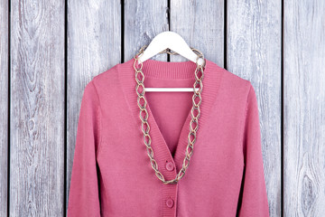 Wall Mural - Flat lay wool coat with accessorie. Pink cardigan with necklace on hanger. Dark wooden desk surface background.