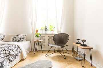 Wall Mural - Modern chair, table with candles and bed with floral blanket in a simple bedroom interior