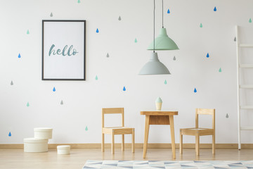 Wall Mural - Lamps above wooden table and chairs in bright kid's room interior with poster on the wall. Real photo