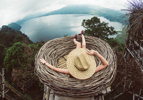 Photographie Back view of a young woman in straw hat relaxing looking the landscape
