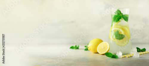 Detox water with mint, lemon on grey background. Banner with copy space. Citrus lemonade. Summer fruit infused water. Refreshing homemade cocktail, selective focus. © jchizhe