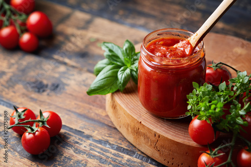 Cuadros en Lienzo Tomato sauce in a glass jar, tomatoes and herbs on its side.