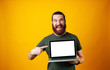 © Vulp - Happy bearded hipster pointing at his blank white screen of the notebook on yellow background.
