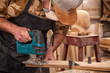 Close up of experienced carpenter in work clothes and small buiness owner  carpenter saw and processes the edges of a wooden bar with a jig saw  in a light workshop