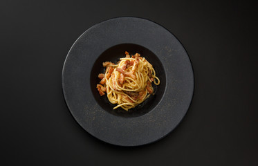 pasta carbonara with bacon in a black plate isolated on a black background