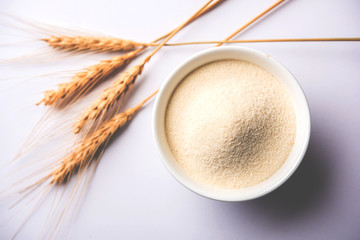 Raw unprepared semolina flour also known as Rava powder in Hindi in bowl or spoon. close-up isolated on white or moody background. selective focus