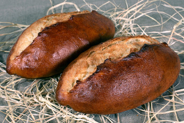 two white bread lying in straw on grey linen tablecloth