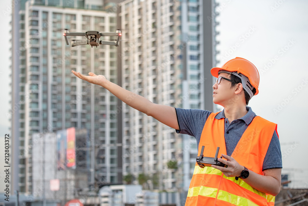 Young Asian engineer flying drone over construction site. Using ...
