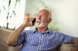 © Mediteraneo - Senior man chatting on a mobile phone while relaxing on a sofa in his living room