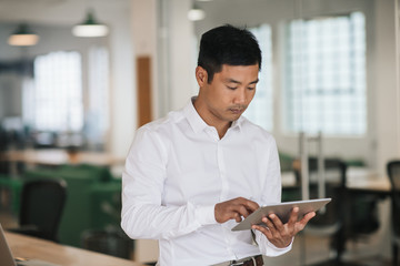 Wall Mural - Focused Asian businessman using a tablet in an office