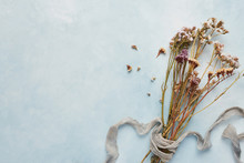 Flat Lay Concept Of Feminine Light Blue Background With Dried Wildflowers Tied With Silk. Top View With Copy Space.