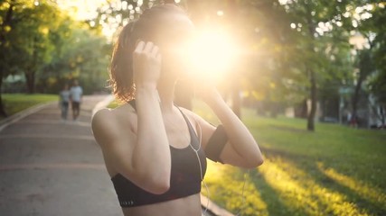 Portrait woman use headphone look at camera smile in park slow motion sun outdoor health hand girl tree sport fitness summer nature internet technology female runner exercise workout young closeup