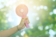 Hand Holding Pink Portable Fan And Green Bokeh Background In Summer, Hot Weather