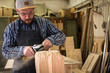 © Виталий Сова - Сarpenter in work clothes and small buiness owner working in woodwork workshop, processes the board with an angle grinder , on the table is a hammer and many tools