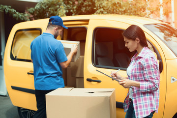 Lady recieving delivery boxes. Beautiful woman putting her signature on digital touchscreen tablet while delivery man gets packages out.