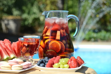 Pool party with sangria pitcher, fruit cocktails and refreshments by the swimming pool. Summer lifestyle, fun and relaxation theme. 
