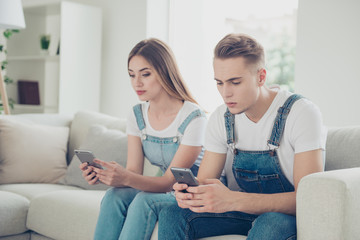 Wall Mural - Young attractive cute couple wearing overall sitting indoor in living room on sofa and texting on their telephones