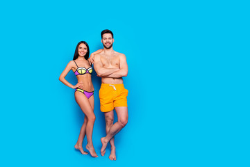 Full-length shot with slim girl in a separate swimsuit laid her hand on shoulder to guy in yellow shorts. The concept of summer vacation, isolated image on a blue background with copy space