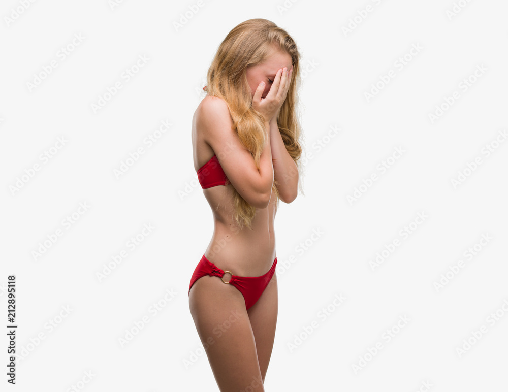 Blonde teenager woman wearing red bikini with sad expression covering face with hands while crying. Depression concept. - obrazy, fototapety, plakaty 