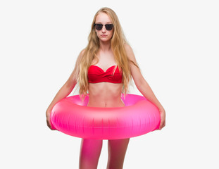 Wall Mural - Blonde teenager woman wearing bikini and holding pink floater with a confident expression on smart face thinking serious