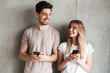 © Drobot Dean - Modern sociable people man and woman smiling while both using mobile phones, isolated over concrete gray wall indoor