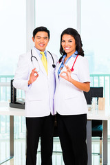 Asian male and female doctor standing proud in his office or medical practice