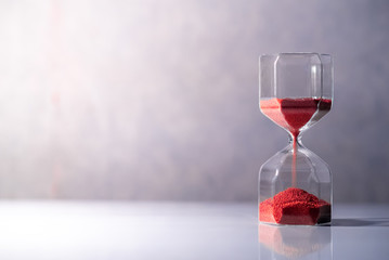 Red sand running through the shape of modern hourglass on white table.Time passing and running out of time. Urgency countdown timer for business deadline concept with copy space