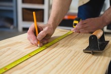 Male Carpenter Measuring And Marking Wood In Workshop