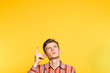 amazed impressed astonished man looking and pointing up with a finger. portrait of a young guy on yellow background popping up or peeking out from the bottom. free space for advertisement.