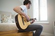 © Wavebreak Media - Man playing guitar in bedroom