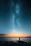 Fototapeta Zachód słońca - Silhouette of a man looking up on stars of the milky way with last light of sunset glows on the horizon