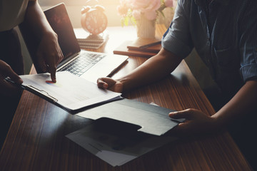 Coworker point finger at paper, annual report, summary, document in office. Notebook, cup of coffee on wooden table. Financial adviser plan and working on laptop. Business and finance concept.