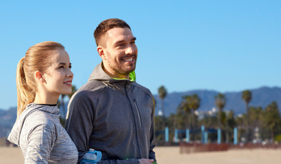 Wall Mural - fitness, sport and people concept - smiling couple with bottles of water over venice beach background in california