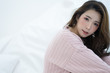 Beautiful Asian young smiling woman warm sweater pink cold and relaxing in bed with copy space . Looking at camera. Model fashion shooting. Autumn, winter season.