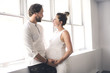 © Louis-Photo - Handsome man and his beautiful pregnant wife standing near the window at home