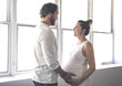 © Louis-Photo - Handsome man and his beautiful pregnant wife standing near the window at home