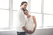 © Louis-Photo - Handsome man and his beautiful pregnant wife standing near the window at home