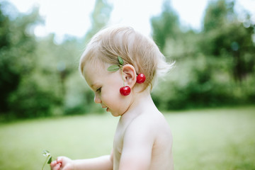 Portrait of cute baby girl with cherries on her ear .