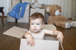 © Tetiana Soares - Close-up portrait of cute little baby boy sitting inside cardboard box dreaming of his future house with big boxes and toys on background, moving out concept