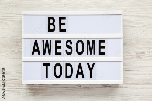 Poster 'Be awesome today' word on lightbox over white wooden background, from above