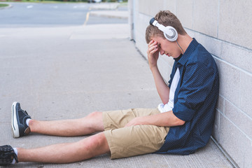 Wall Mural - Upset teen sitting on the ground against a wall while listening to music.