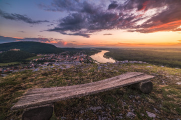 Wall Mural - View of Small City of Hainburg an der Donau with Danube River as Seen from Braunsberg Hill at Beautiful Sunset. Wooden Bench in Foreground.