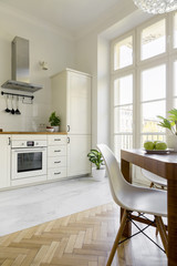 White chair at wooden dining table in simple kitchen interior with window. Real photo