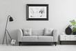 © Photographee.eu - Framed photo on a wall above a fancy, gray sofa with cushions in a minimalist living room interior and place for a table. Real photo.