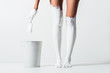 Leinwandbild Motiv cropped image of woman with legs painted with white paint holding brush above bucket on white