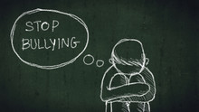 Sad Young Boy Sitting On The Floor With Text Stop Bullying Written With Chalk On Chalkboard. Social Problems Of Humanity