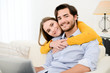 © W PRODUCTION - cheerful young couple on sofa at home websurfing and shopping online with laptop computer internet technology